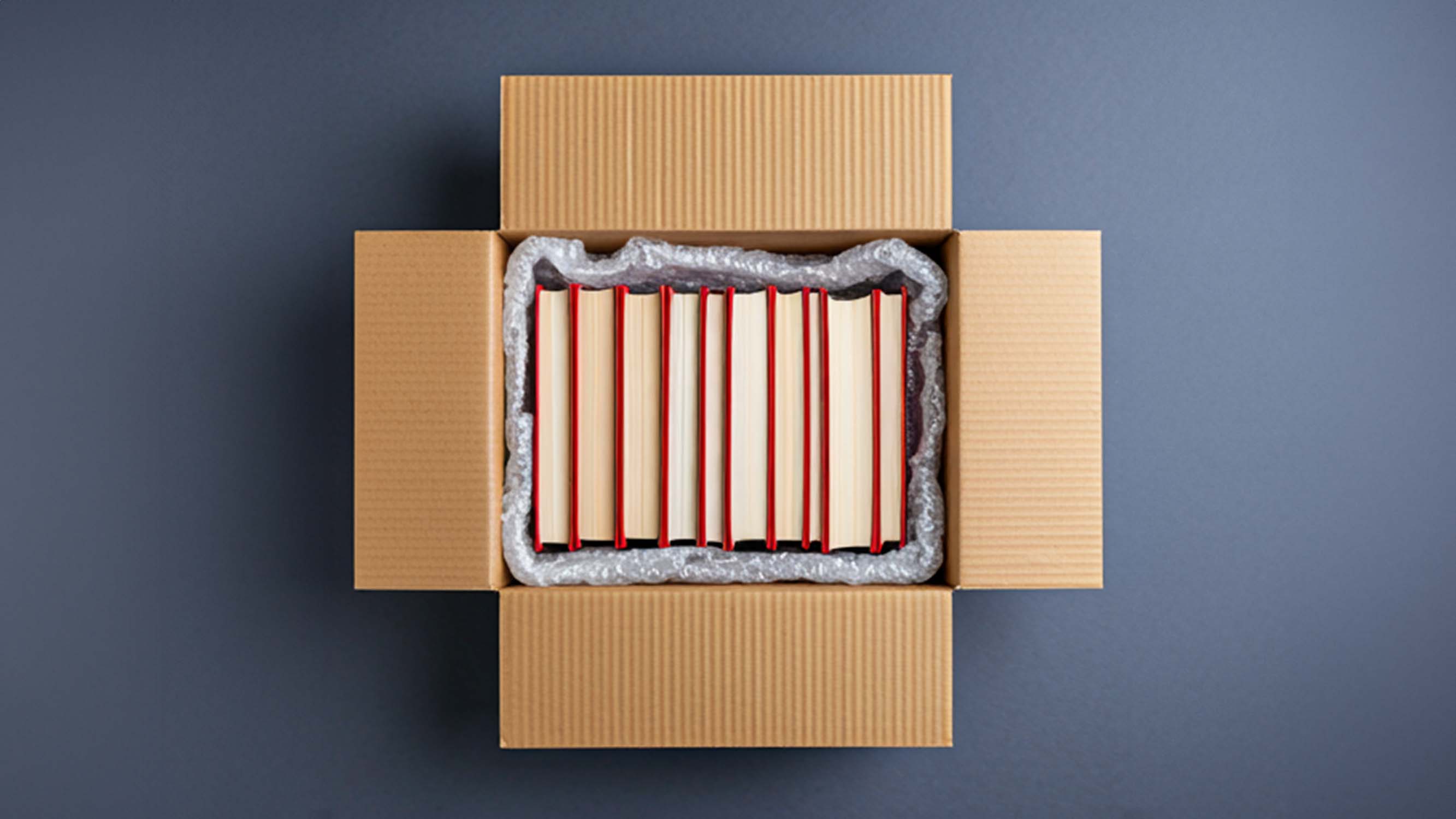 An open box filled with books surrounded by void fill materials like kraft paper and bubble wrap.